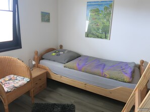 A single bed with a wooden frame, a small bedside table, a chair with a cushion, and a wall-mounted picture. - Holiday Home 'Haus "Marschenring"' with Private Terrace, Private Garden and Wi-Fi (Butjadingen)