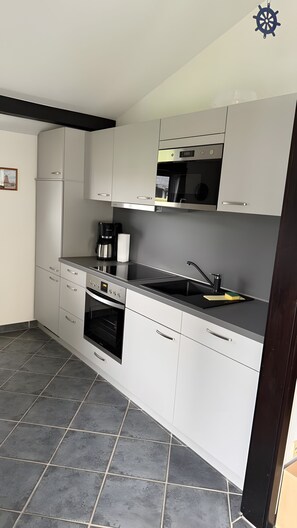 A modern kitchen with white cabinets, a stainless steel range, a built-in oven, and a black countertop. - Holiday Home 'Haus "Marschenring"' with Private Terrace, Private Garden and Wi-Fi (Butjadingen)