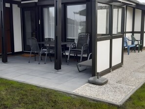 An outdoor patio with a table and chairs, a covered seating area, and a view of the house in the background. - Holiday Home 'Haus "Marschenring"' with Private Terrace, Private Garden and Wi-Fi (Butjadingen)