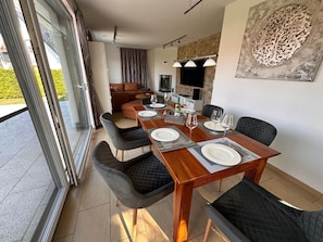 A dining area with a wooden table set for four, surrounded by chairs, a sofa, and a television. - Villa Ambiente am See (Goehren-Lebbin)