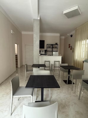 A modern dining area with multiple tables and chairs, a kitchen area with appliances, and a staircase leading to another level. - Hotel Pigalle (Bellaria-Igea Marina)