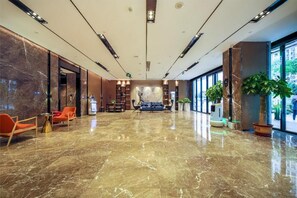 A spacious lobby with a marble floor, seating area with chairs, a sofa, and a reception desk. - Echarm Hotel (Heyuan)