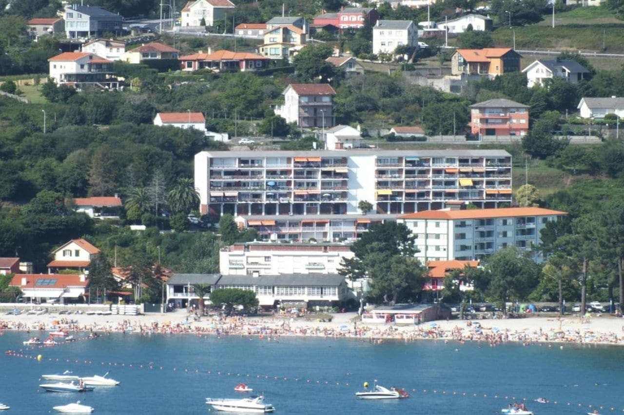 Un hôtel situé sur la côte, avec plusieurs étages, une plage en premier plan et plusieurs bateaux sur l’eau.