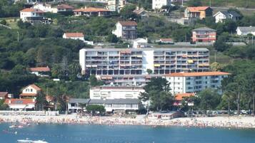 Un hôtel situé sur la côte, avec plusieurs étages, une plage en premier plan et plusieurs bateaux sur l’eau.