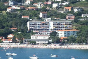 A coastal hotel with multiple floors, a beach in the foreground, and several boats on the water.