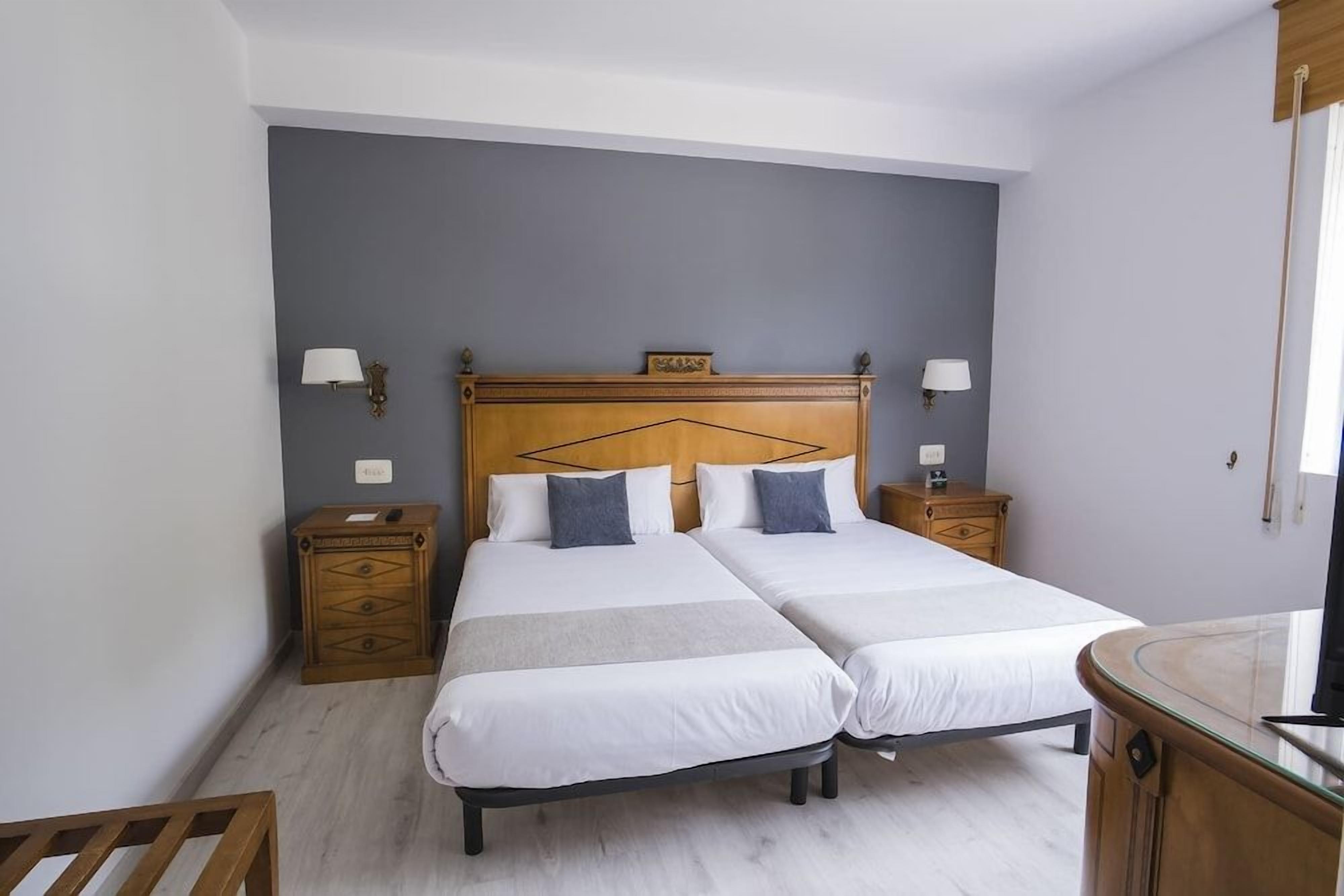 Ein Doppelbett mit Holz Kopfteil, zwei Nachttische mit Lampen sowie ein kleiner Holzschrank.