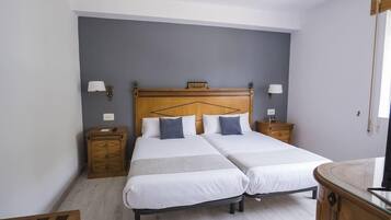 Ein Doppelbett mit Holz Kopfteil, zwei Nachttische mit Lampen sowie ein kleiner Holzschrank.