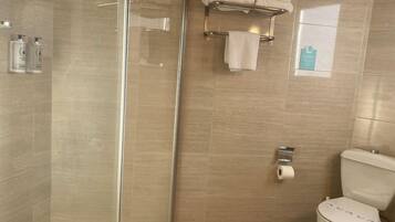 Une salle de bain avec une douche à parois de verre, des toilettes et un porte-serviettes avec des serviettes pliées.