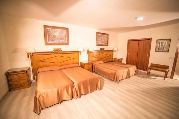 Quarto de hotel com duas camas, um guarda-roupa de madeira, um banco e quadros nas paredes.