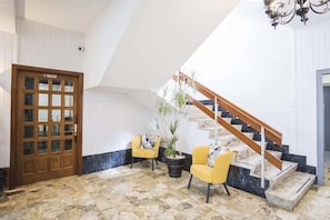A room with a wooden door, a staircase with a wooden handrail, and two yellow chairs with a potted plant. - Hotel Iberia (Cabanas)