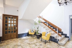 Una habitación con puerta de madera, una escalera con barandilla de madera y dos sillas amarillas con una planta en maceta.