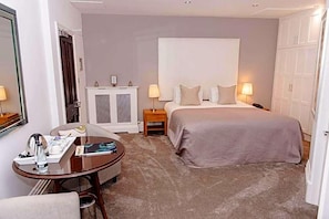 A hotel room with a bed, bedside tables, a round table with a chair, a wardrobe, and a mirror. - Woodlands Hotel (Leeds)