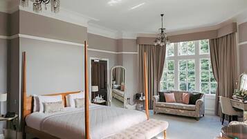 A four-poster bed with a bench, a sofa, a desk, and a large window with curtains.