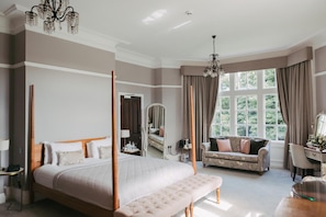 A bedroom with a four-poster bed, a sofa, a desk, and a large window with curtains. - Woodlands Hotel (Leeds)