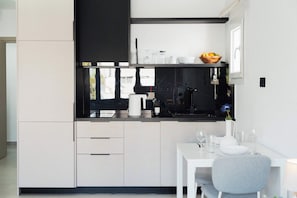 Una cocina moderna con encimera negra, armarios blancos, una cafetera y un comedor con mesa y sillas.