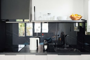 A modern kitchen with a black countertop, a coffee machine, and a bowl of fruit on the shelf. - Modern Central Studio Walk to Beach & Dining (Lemesos)