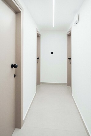 A corridor with doors on both sides, a light fixture on the ceiling, and a small square object on the floor. - Modern Central Studio Walk to Beach & Dining (Lemesos)