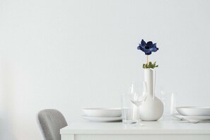 A white dining table with a white vase containing a blue flower, a glass, and a bowl. - Modern Central Studio Walk to Beach & Dining (Lemesos)