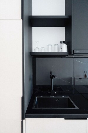 Une cuisine moderne dotée d’un plan de travail noir, d’un évier en acier inoxydable et d’un réfrigérateur de la marque Midea.
