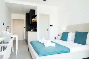 A hotel room with a bed, a desk, a chair, and a kitchenette. - Modern Central Studio Walk to Beach & Dining (Lemesos)