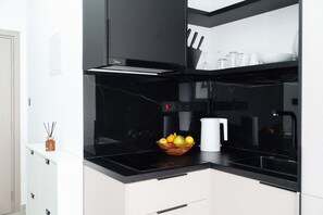 Una cucina moderna con un piano di lavoro nero, un bollitore bianco e una ciotola di frutta.