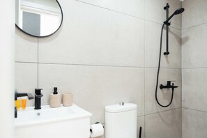 Un bagno con lavandino bianco, toilette e doccia con tubo nero.