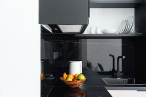 A modern kitchen with a black countertop, a wooden bowl of fruit, and a white appliance. - Modern Central Studio Walk to Beach & Dining (Lemesos)