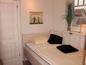 Ein Schlafzimmer mit Bett, Nachttisch, Lampe, Fenster und einem Bild an der Wand.