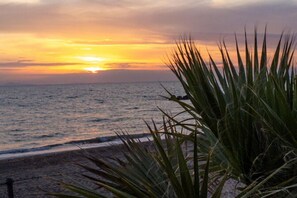 Un sol ponent sobre l'oceà amb una platja al primer pla.