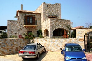 A stone building with a tower, a car parked in front, and a gate. - Mani Village Villas (West Mani)