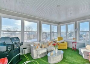 A sunroom with a large window, a grill, a sofa, and a chair. - Modern 2BR Condo in Mirabel-Cozy & Stylish Retreat (Mirabel)