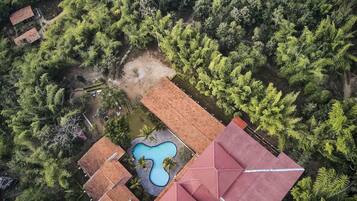An aerial view of a property with multiple buildings, a swimming pool, and dense surrounding vegetation.