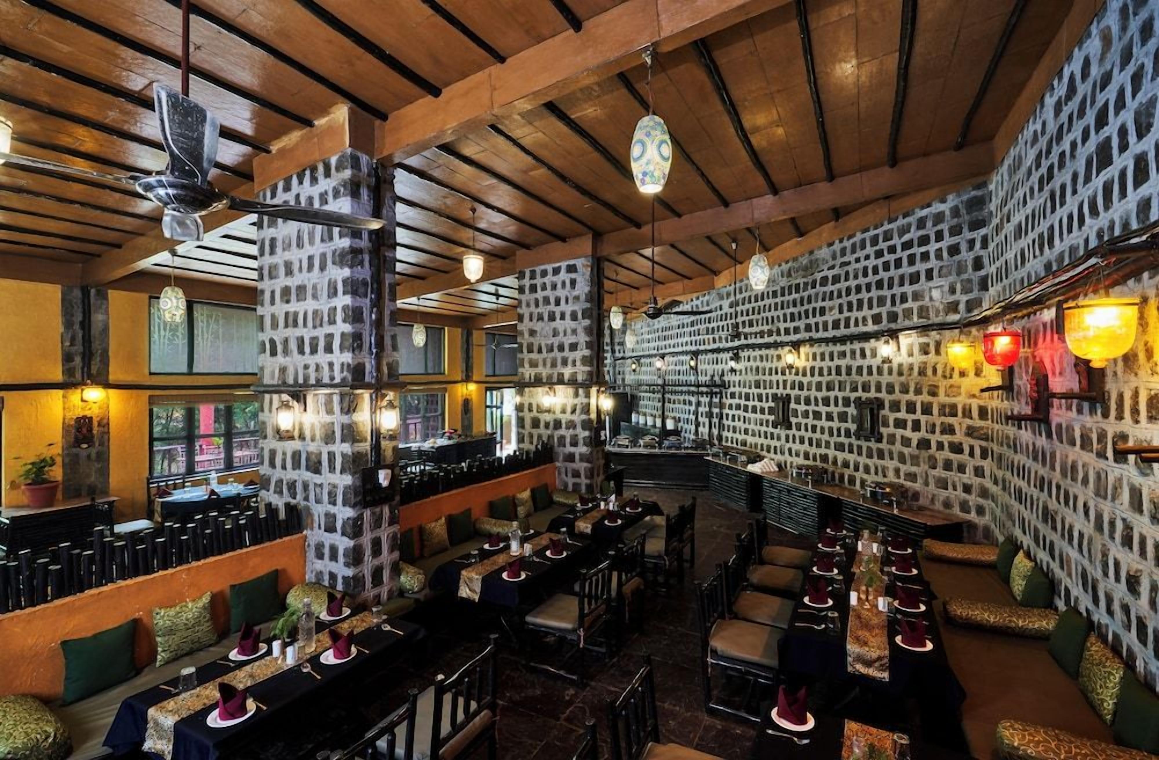 A restaurant with high ceilings, exposed beams, and a stone wall. Tables are set with red napkins and white plates.