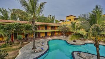 A hotel with a swimming pool, palm trees, and a yellow building.