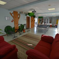 Una stanza con attrezzature per esercizi, un tavolo da ping pong e sedie rosse.