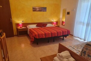 Una camera d'albergo con un letto, abat-jour, comodino, una sedia e una finestra con tende.