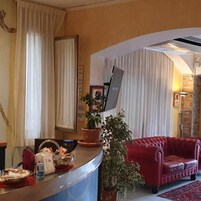 Un'area di accoglienza con un banco reception, un divano rosso e una pianta in vaso.
