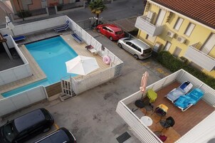 Vista aerea di una zona residenziale con piscina, un'auto rossa e un'auto argento parcheggiate vicino a un edificio giallo.