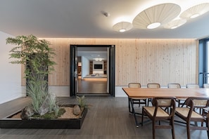 A modern interior with a wooden dining table and chairs, a plant, and a view into a living area. - Denbasta Ryokan Hotel (Geoje)