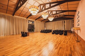 Una habitación amplia con suelo de madera, techo alto con vigas a la vista y varias sillas negras dispuestas para sentarse.