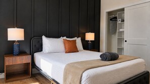 A neatly made bed with white bedding, two bedside tables with lamps, a dark headboard, and a wardrobe with hanging space. - The James Suite Two | New 2BR Beach Block (Atlantic City)