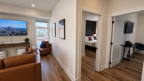 A modern living room with a large flat-screen TV, a brown leather sofa, and a wooden floor. - The James Suite Two | New 2BR Beach Block (Atlantic City)