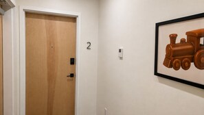 A hallway with a wooden door, a wall-mounted number '2', a wall-mounted light switch, and a framed picture of a train. - The James Suite Two | New 2BR Beach Block (Atlantic City)