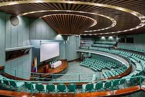 Un salón de conferencias con asientos escalonados, un atril y una pantalla grande.