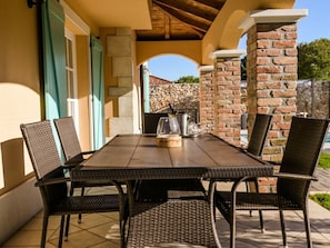 An outdoor patio with a table and chairs, a stone wall, and a view of a stone building. - Villa in Kras, Dobrinj With Swimming Pool (Dobrinj)