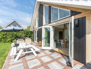 A modern house with a patio, outdoor furniture, and a dining area visible through glass doors. - The Beach Forest House (Burgh-Haamstede)