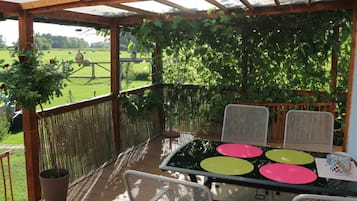 Une terrasse extérieure avec une table et des chaises, entourée d’une pergola en bois et offrant une vue sur un champ verdoyant.