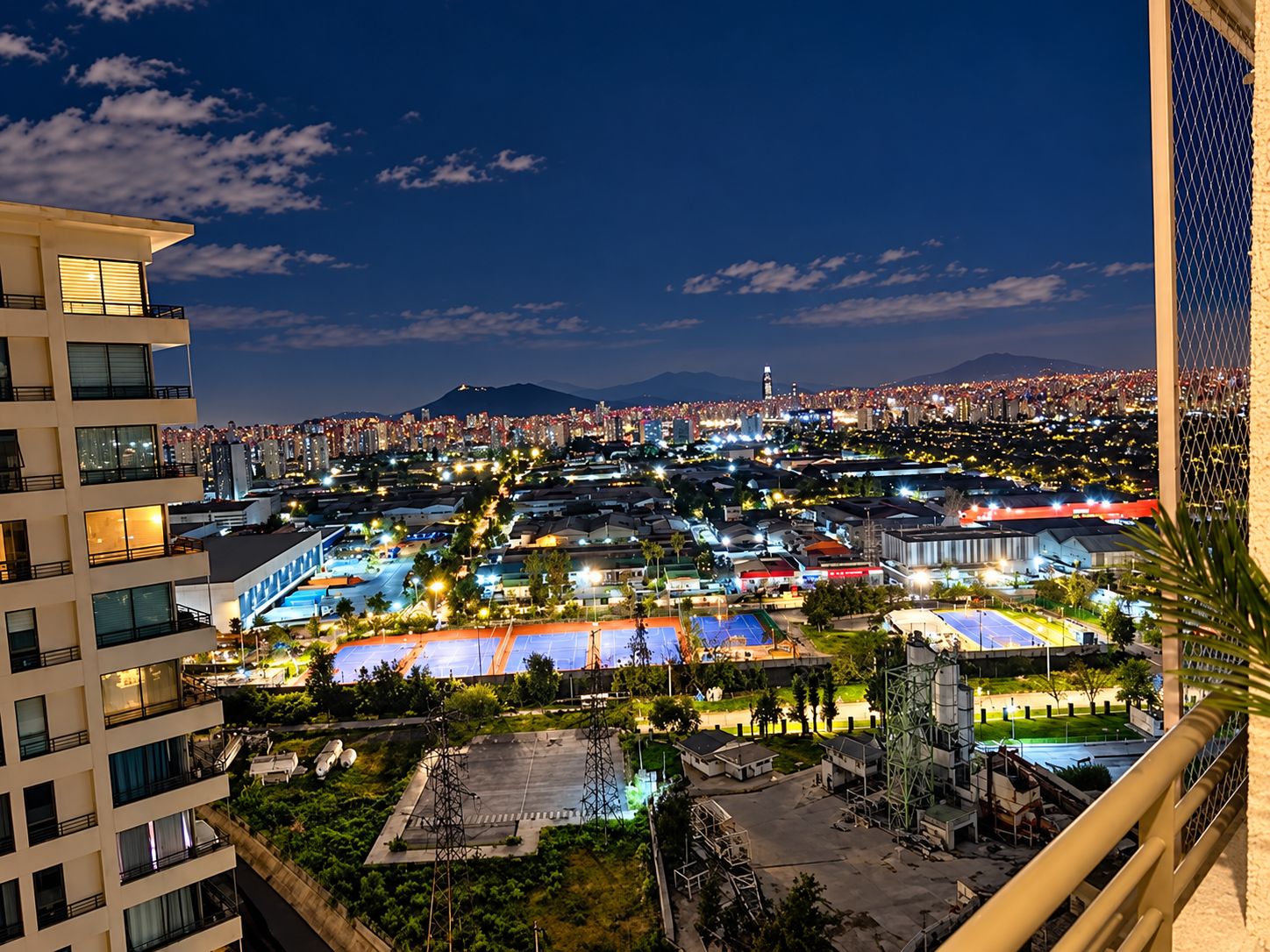Un hotel alt amb vista a un paisatge urbà nocturn, amb edificis il·luminats i una muntanya a la distància.
