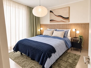 A modern bedroom with a large bed, a wooden headboard, a wall-mounted abstract painting, and two bedside lamps.