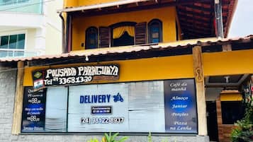 Un edificio con un letrero de servicio de entrega, un número de contacto y un menú que ofrece café, desayuno y pizza.